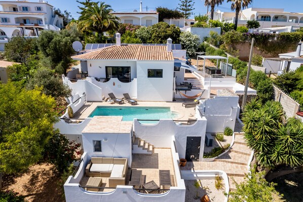 A modern villa with a swimming pool, outdoor seating, and a view of neighboring buildings.