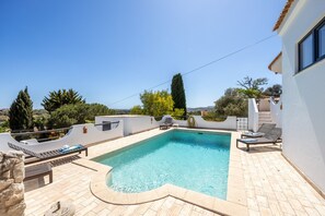 A rectangular swimming pool with a curved edge, surrounded by a tiled deck.
