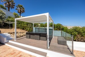 An outdoor seating area with a pergola, wicker furniture, and a glass railing.