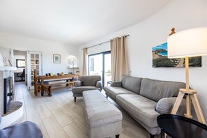 A modern living room with a sofa, ottoman, and a dining area with a table and chairs.