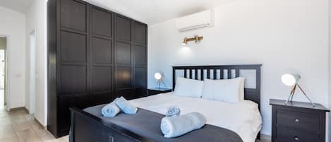 A modern bedroom with a large bed, dark wood wardrobe, bedside tables with lamps, and a ceiling-mounted light fixture.