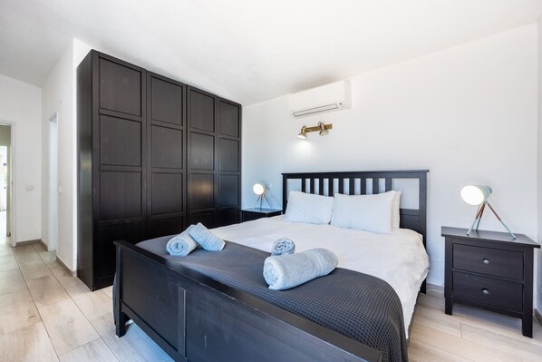 A modern bedroom with a large bed, dark wood wardrobe, bedside tables with lamps, and a ceiling-mounted light fixture.