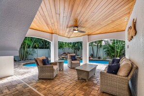 A covered patio area with wicker furniture, a ceiling fan, and a view of a swimming pool. - Above it All: Rooftop Deck Gulf Views, Pool, 5 Homes to Beach by Anna Maria Life Vacation Rentals (Holmes Beach)
