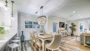 Une cuisine spacieuse avec une table à manger en bois, des meubles blancs et des luminaires suspendus.