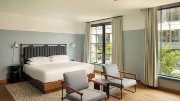 Habitación de hotel con cama, dos sillones, una mesita, lámpara y ventana con cortinas.