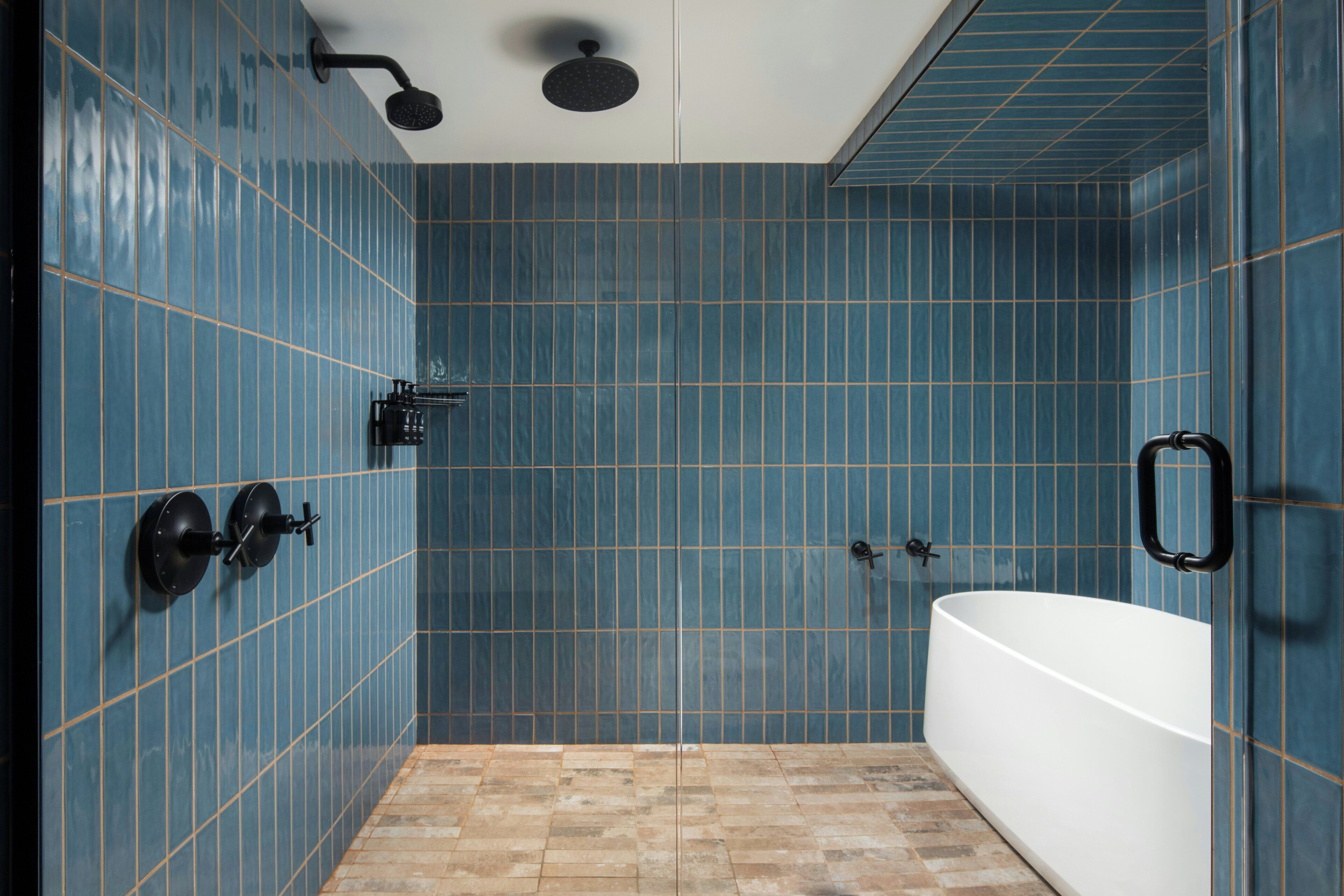 A bathroom with blue tiled walls, a white bathtub, and a shower with a handheld showerhead.
