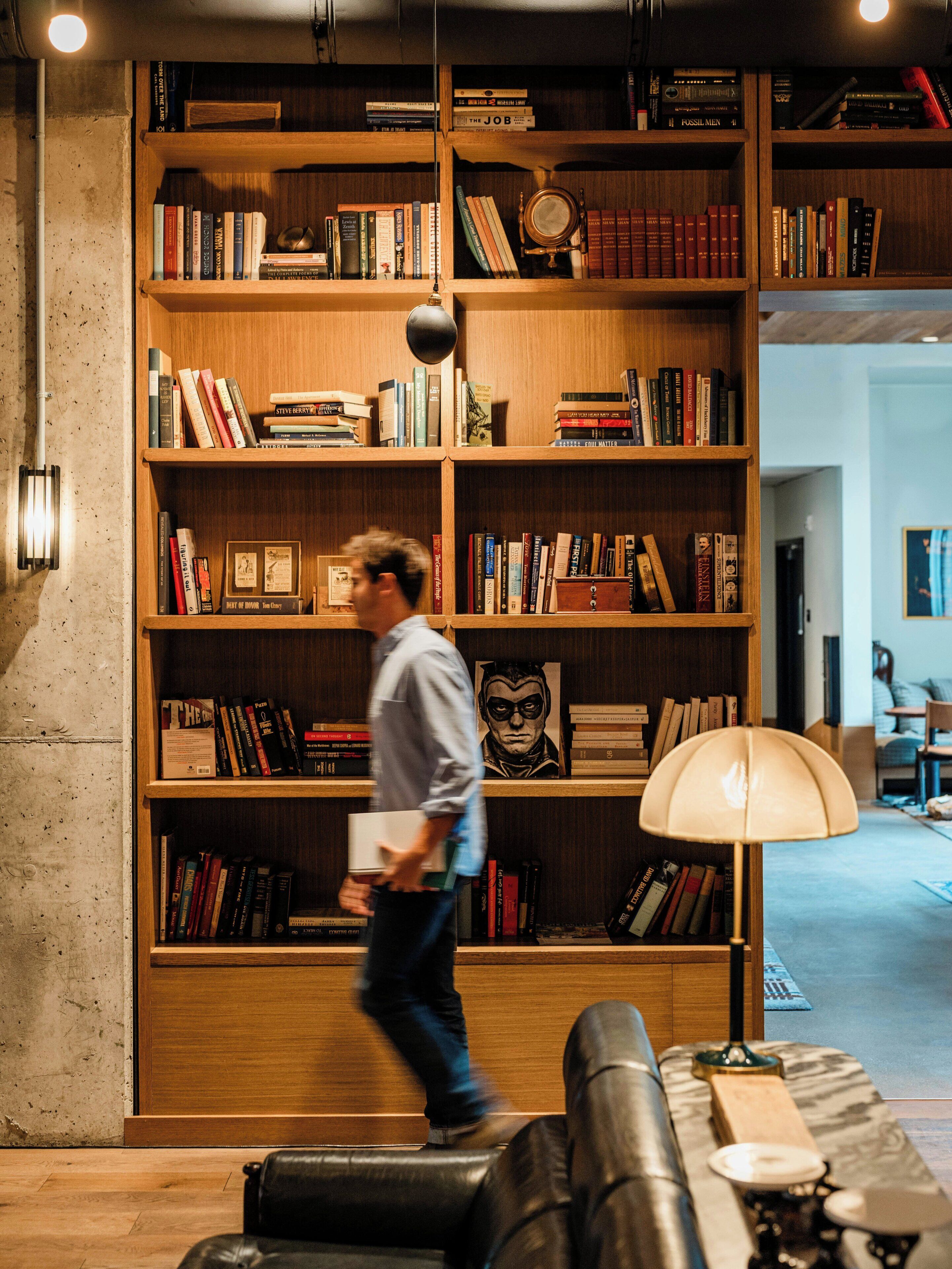 Una habitación con una amplia estantería de madera llena de libros, un sofá de cuero y una lámpara.