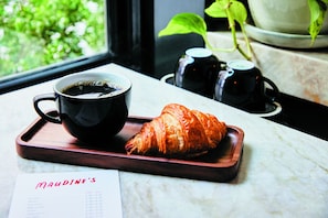A croissant and a cup of coffee on a tray, with a menu and a window view of greenery.