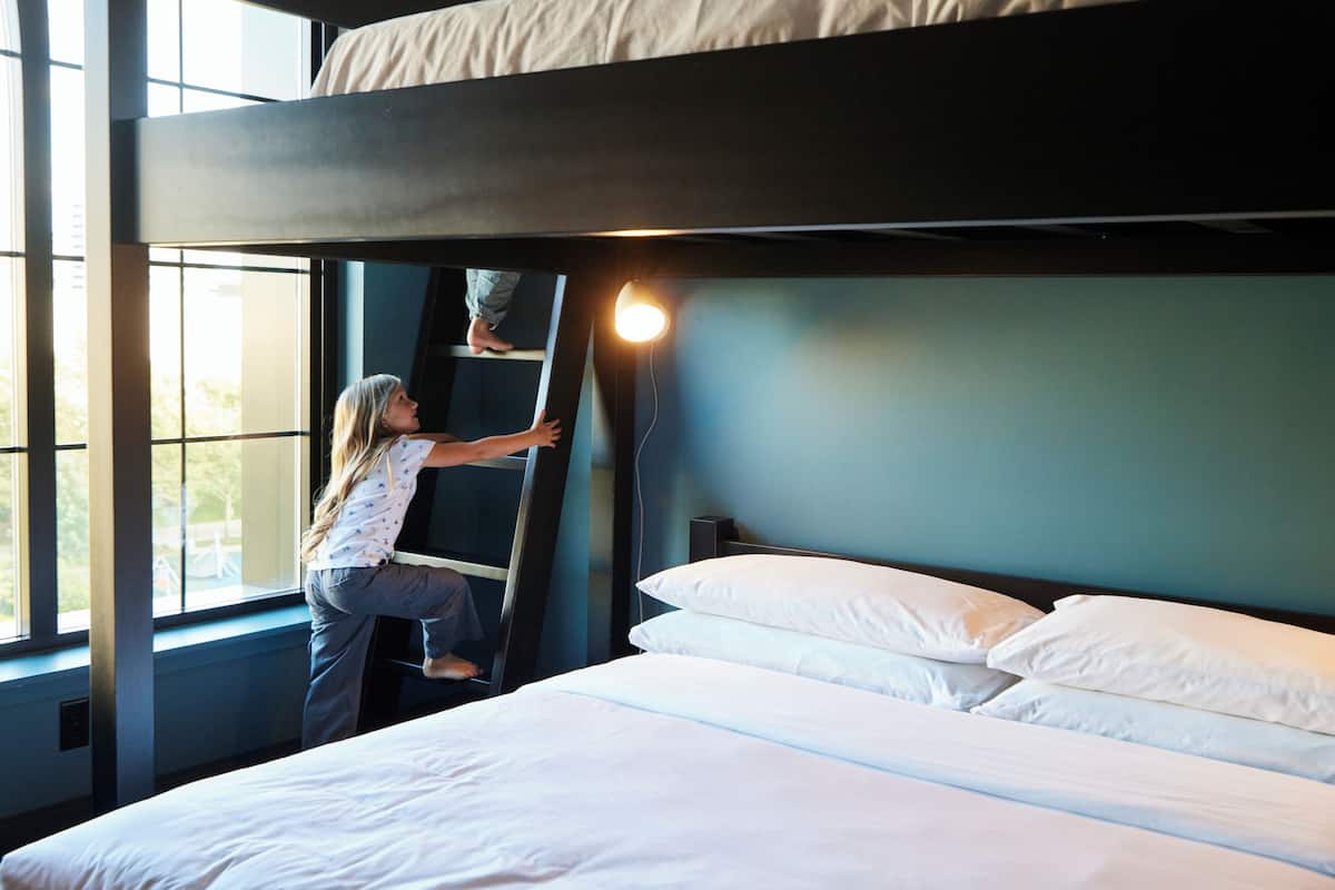 A bunk bed with a ladder, a window, and a bed with white bedding.