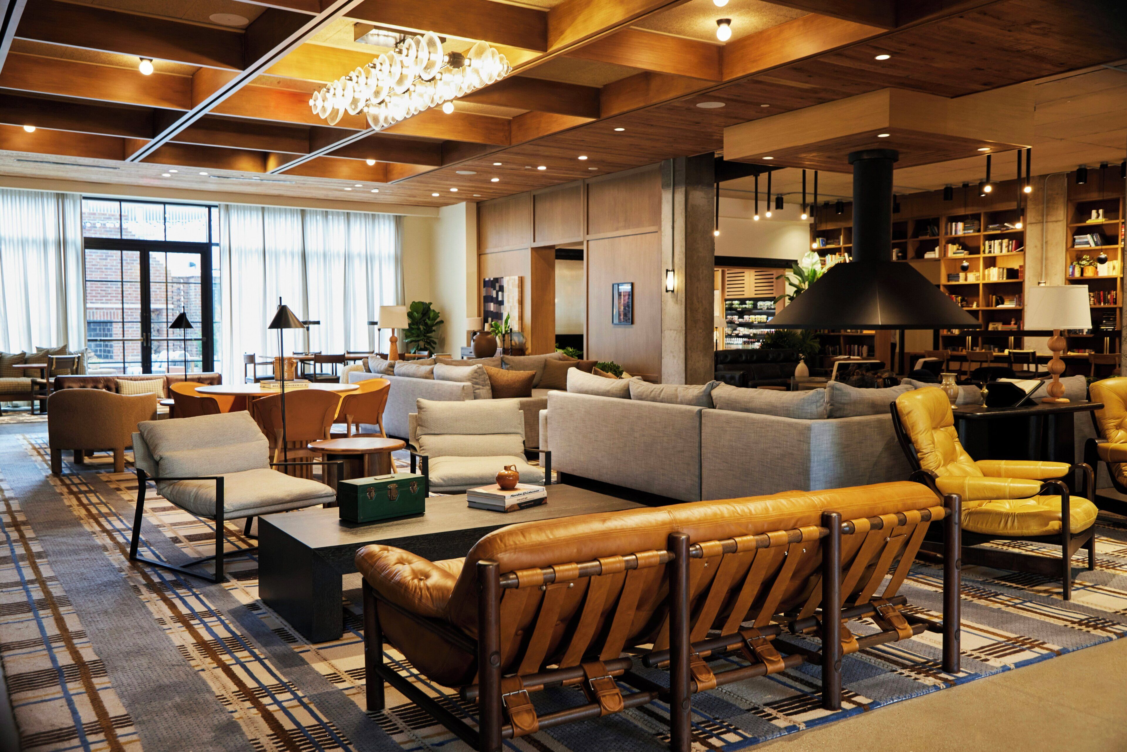 Een ruime hotellobby met een grote bank, fauteuils, een salontafel en een boekenplank vol boeken.