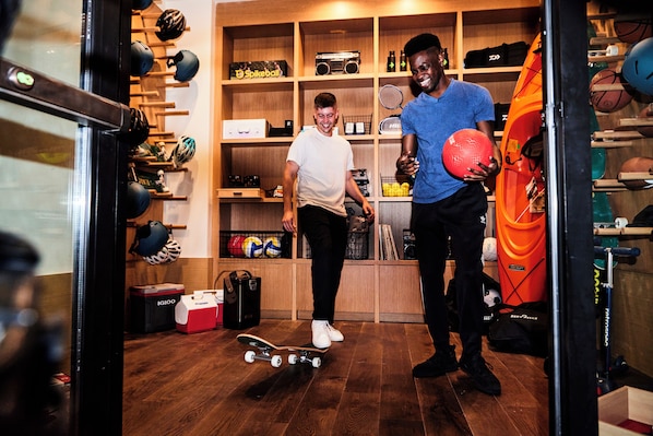 A room with wooden flooring, a skateboard, and a person holding a volleyball.