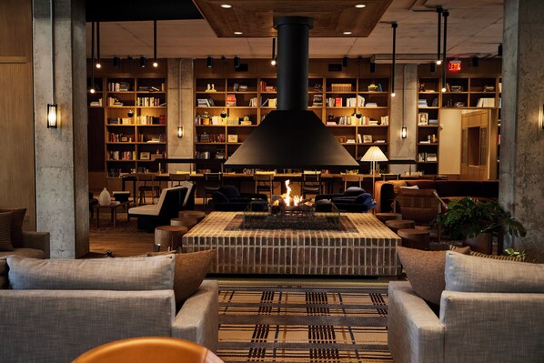 A cozy lounge area with a fireplace, comfortable seating, and a large bookshelf filled with books.