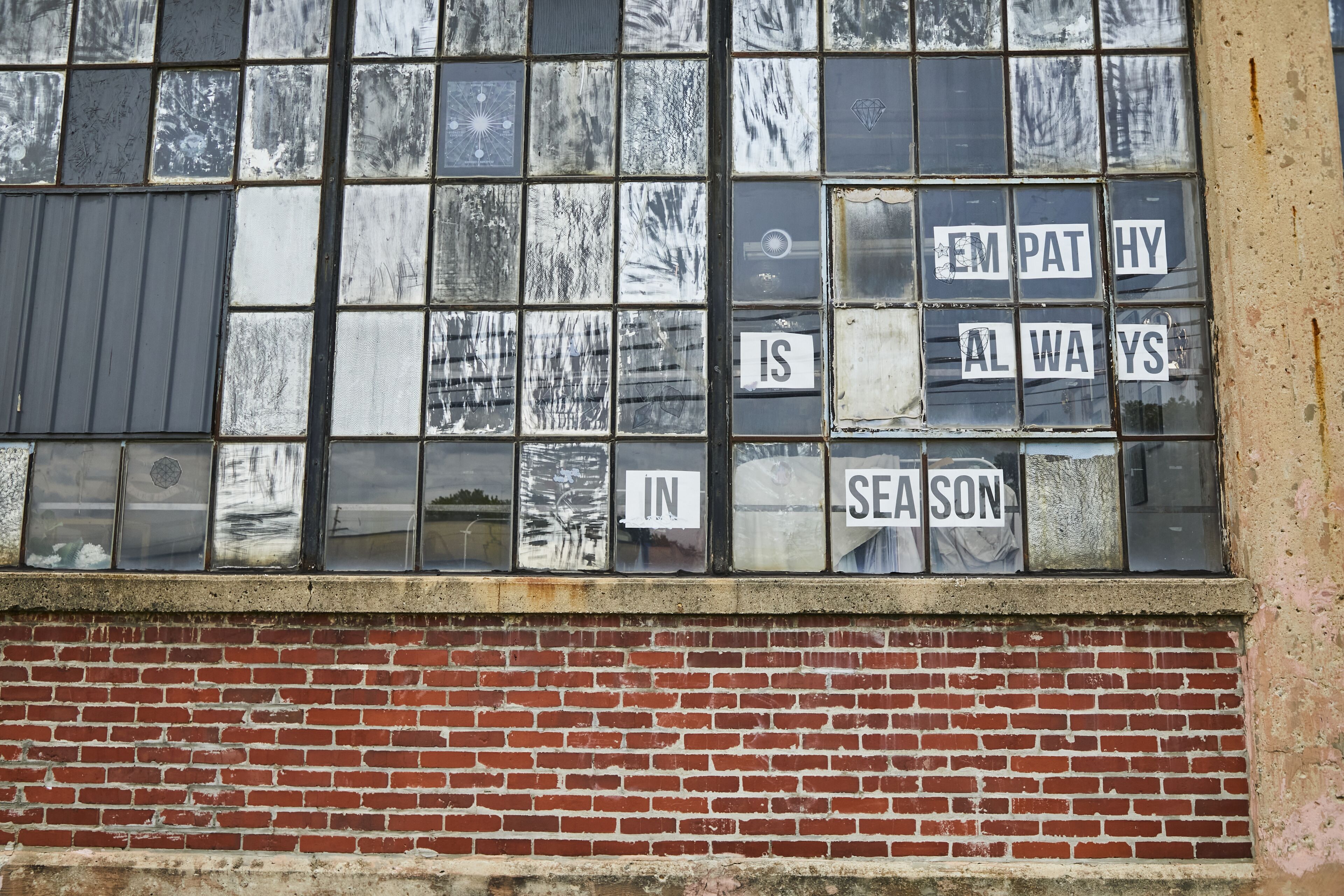 A window with multiple panes, some with stickers that read "EMPATHY IS ALWAYS IN SEASON".