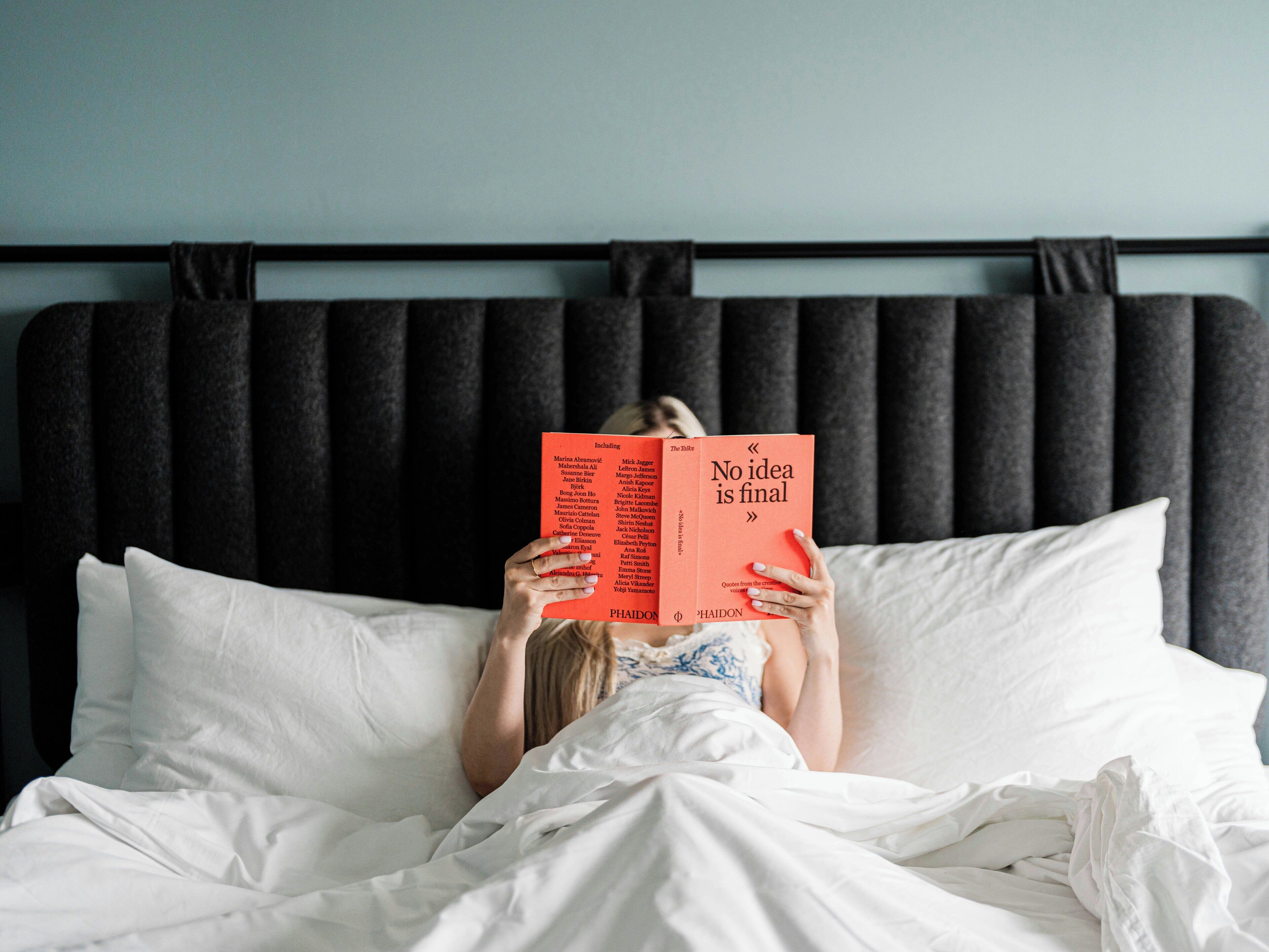 Una persona acostada en la cama leyendo un libro que se titula 'No idea is final'.