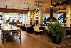 En rymlig entréhall med en lång, träinredd receptionsdisk, flera sittgrupper, en stor bokhylla och en trappa i bakgrunden.