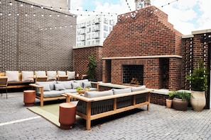 Relax in a cozy seating area with a sofa, bench, and small table, surrounded by potted plants and a brick fireplace.
