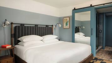 A neatly made bed with white linens, a bedside table with a book, and a wall-mounted lamp.