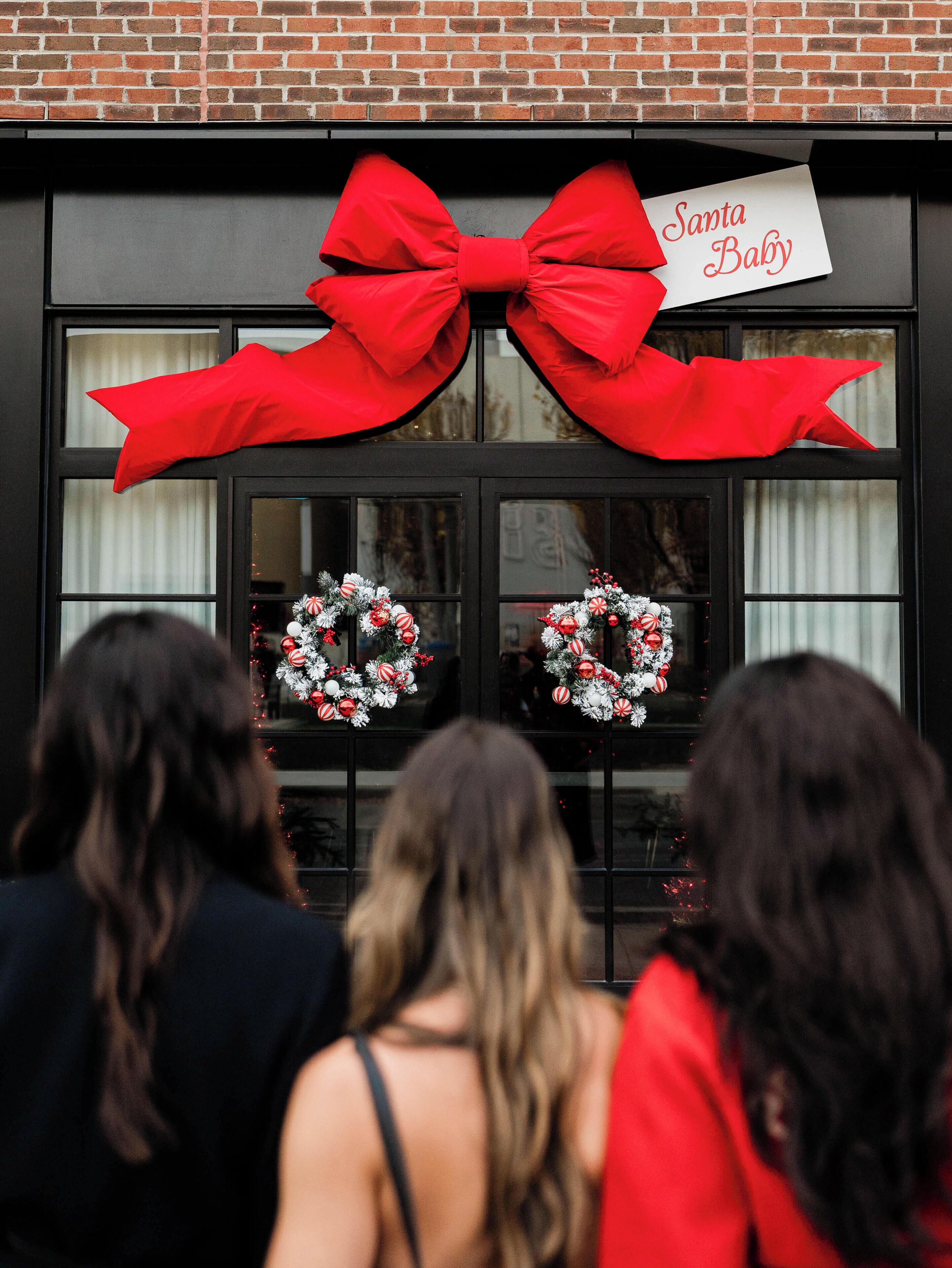 A building facade with a large red bow decoration and two wreaths on the windows.