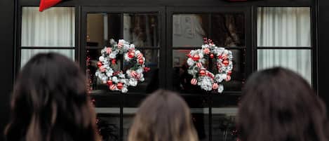 A building facade with a large red bow decoration and two wreaths on the windows.