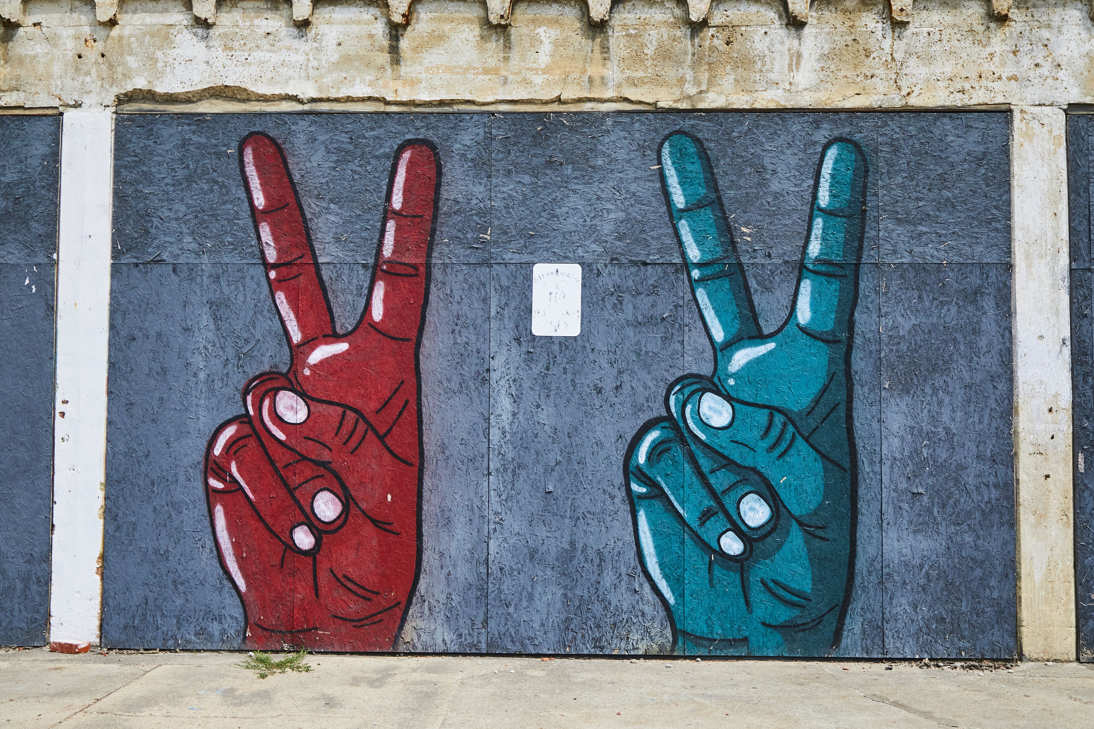 A wall with two hand-painted peace signs, one red and one blue, on a grey background.