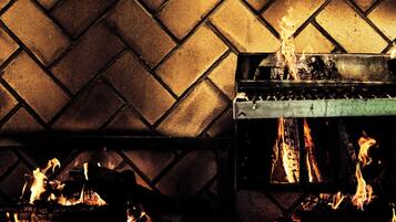 A fireplace with a herringbone-patterned wall and logs burning.