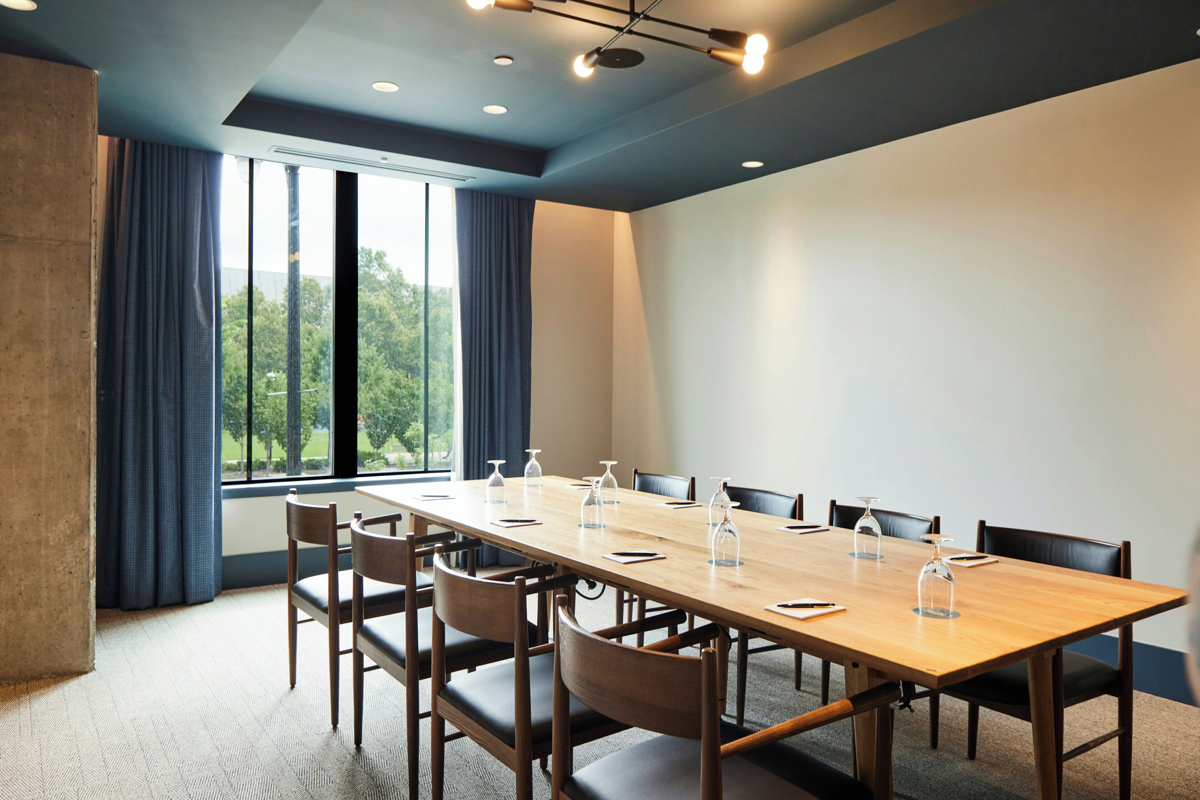 A conference room with a long table, chairs, and a view of trees through large windows.
