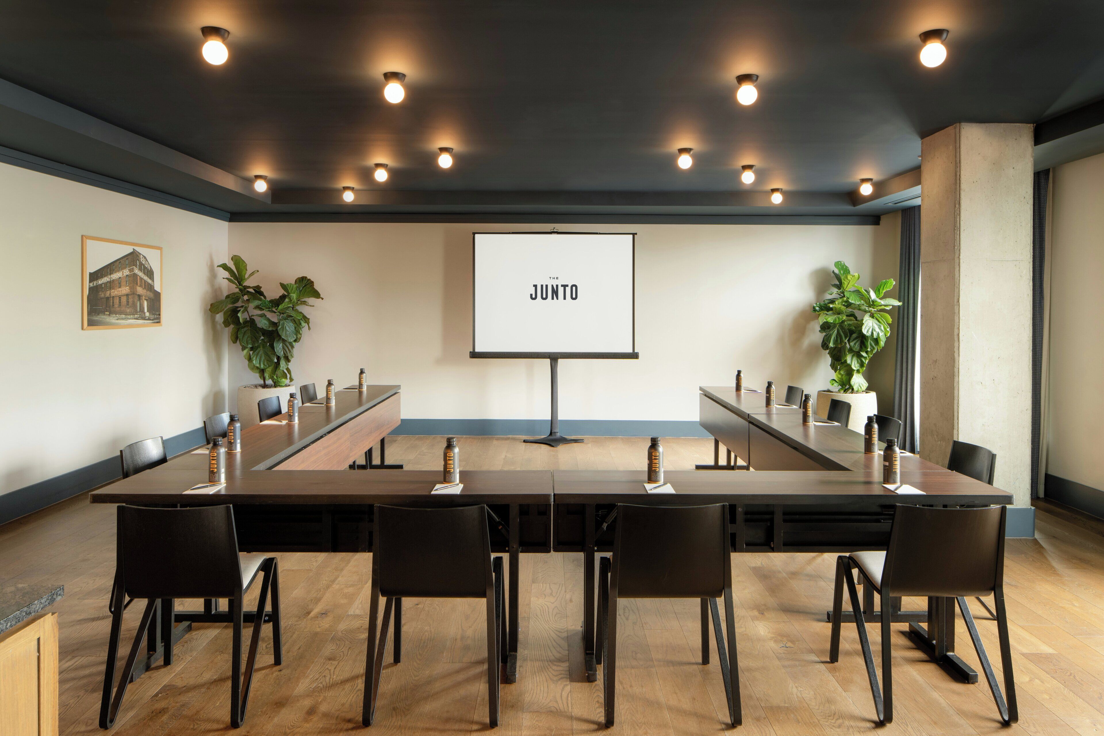 A conference room with a long table, chairs, a projector screen, and plants.