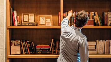 A person reaching for a book on a wooden bookshelf filled with various books.