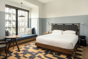 A hotel room with a large bed, a seating area with a table, and a view through a window.