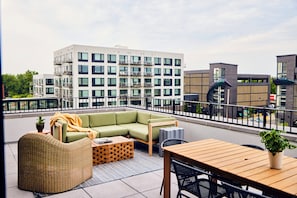 Relax on the rooftop terrace with a green sectional sofa and wicker armchair, surrounded by a city view.
