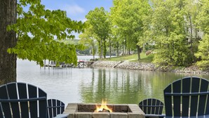 Un área de estar junto al lago con un hogar de piedra y sillas tipo Adirondack.
