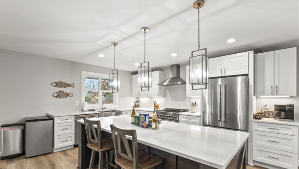 Una cocina moderna con armarios blancos, electrodomésticos de acero inoxidable y una isla central con taburetes de bar.