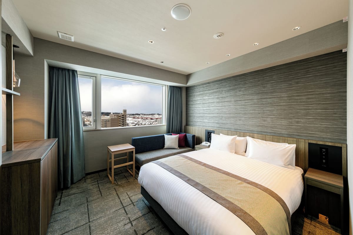 Hotellihuone, jossa on suuri sänky, työpöytä, tuoli, yöpöytä ja näkymä kaupunkiin.
