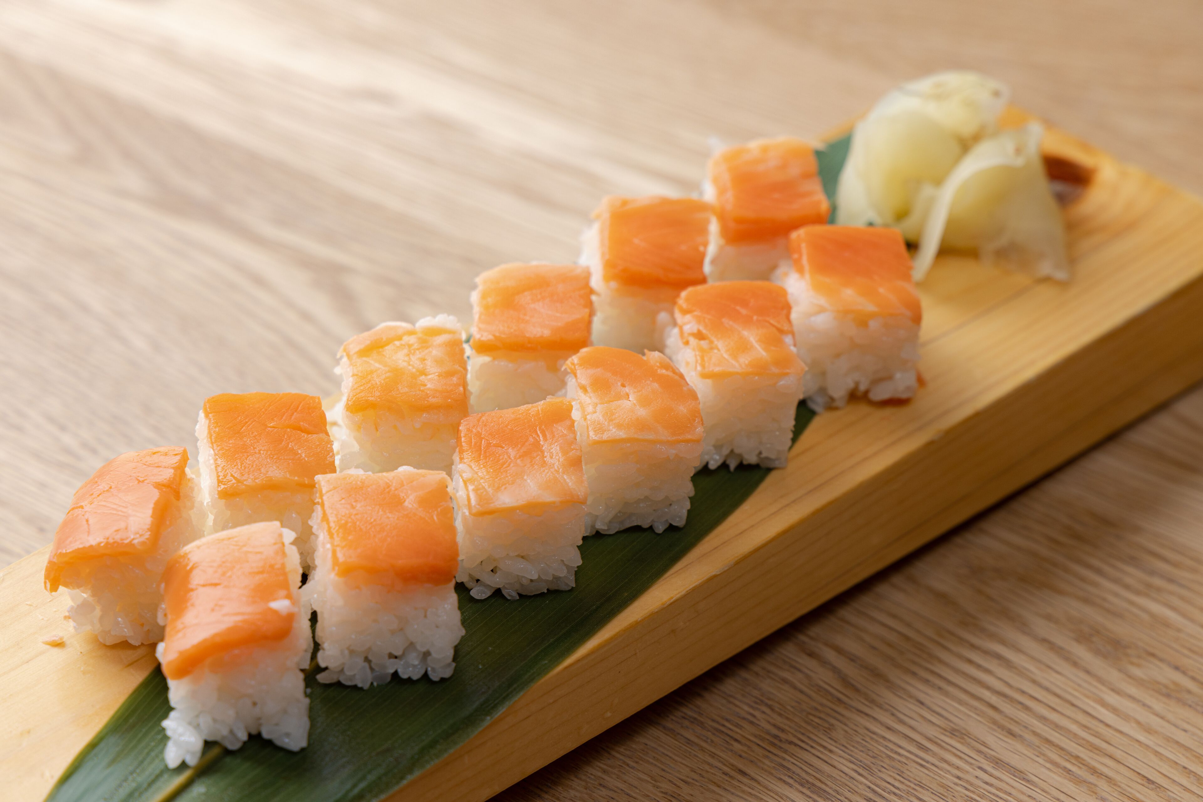 A wooden serving board with sushi pieces arranged in a line.