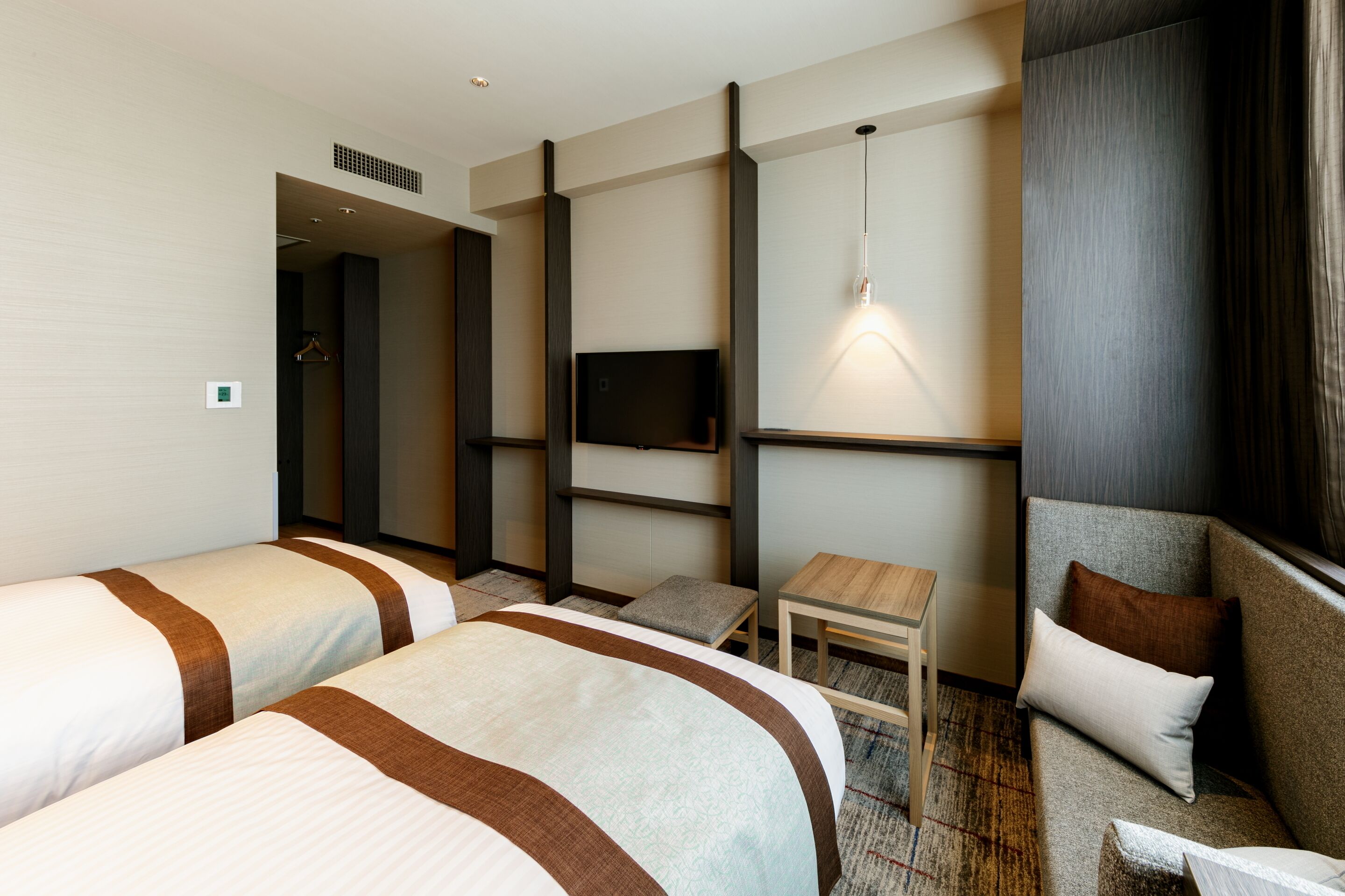 Quarto de hotel com duas camas, uma televisão, uma mesa pequena e um espaço de estar.