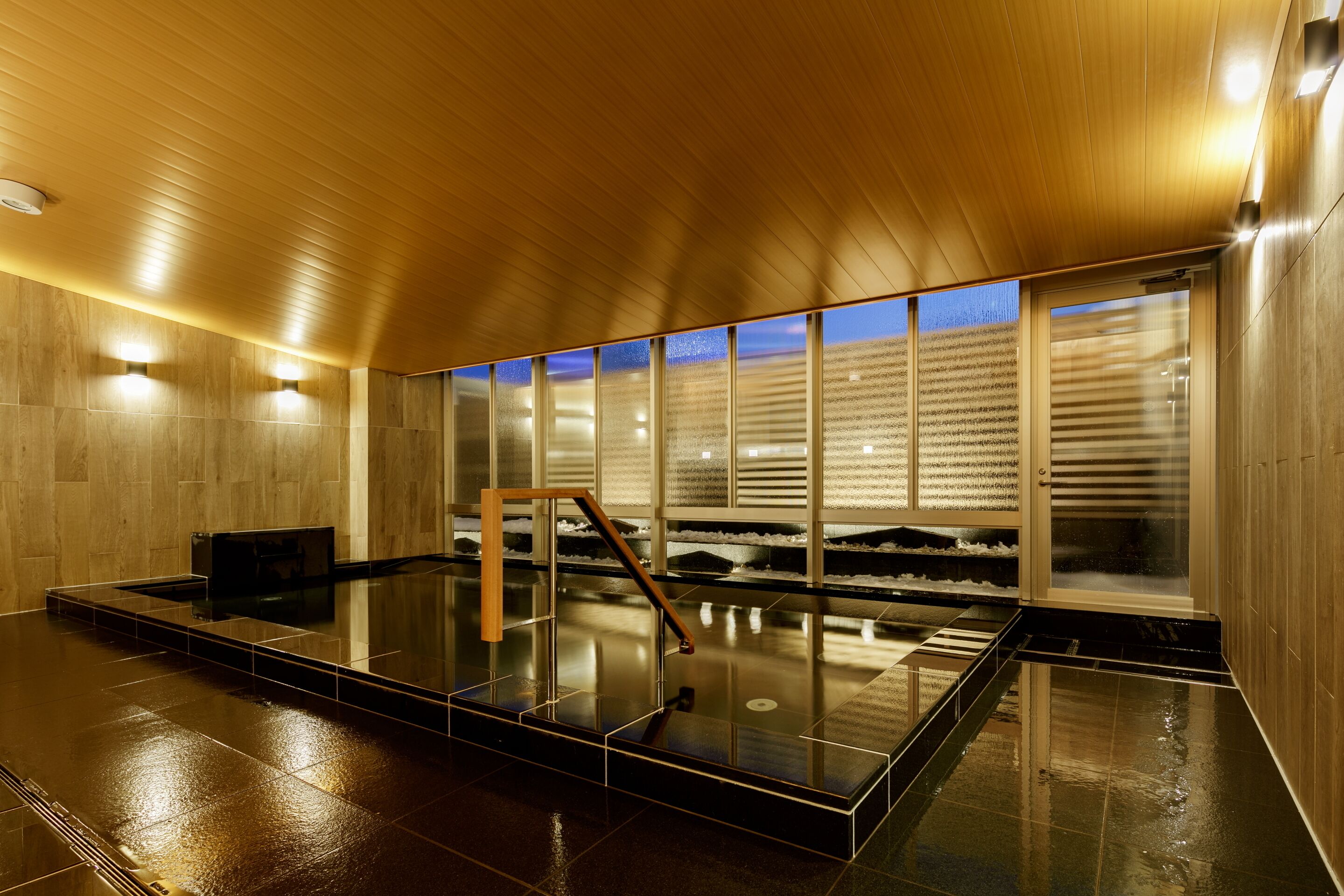 Un espacio interior moderno con techo de madera, pared de vidrio con vistas y suelo reflectante.