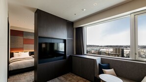 A modern hotel room with a bed, a TV, a seating area, and a large window offering a city view. - HOTEL VISCHIO TOYAMA by GRANVIA (Toyama)