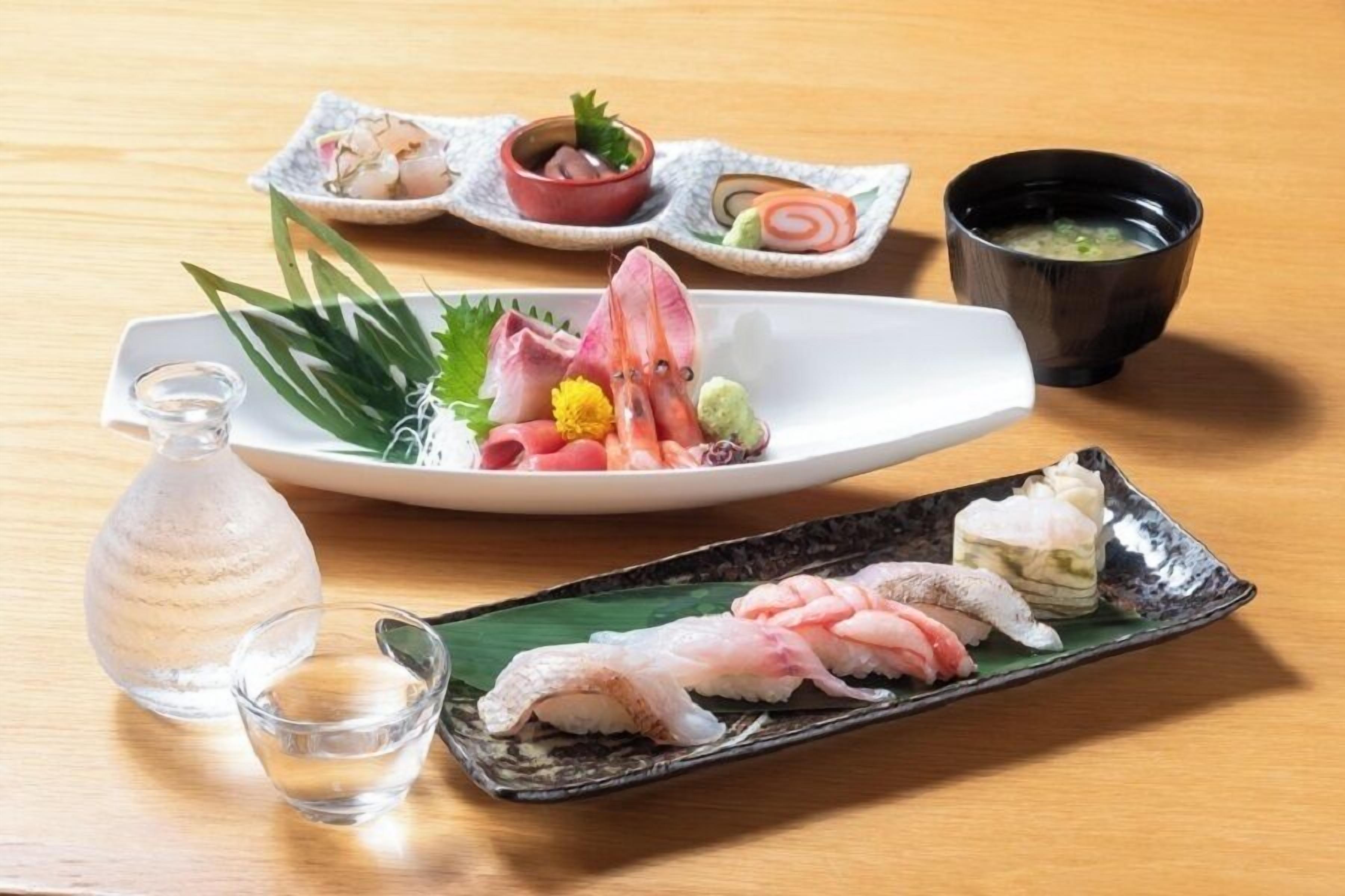 A table with various dishes, including sashimi and a bottle of sake.
