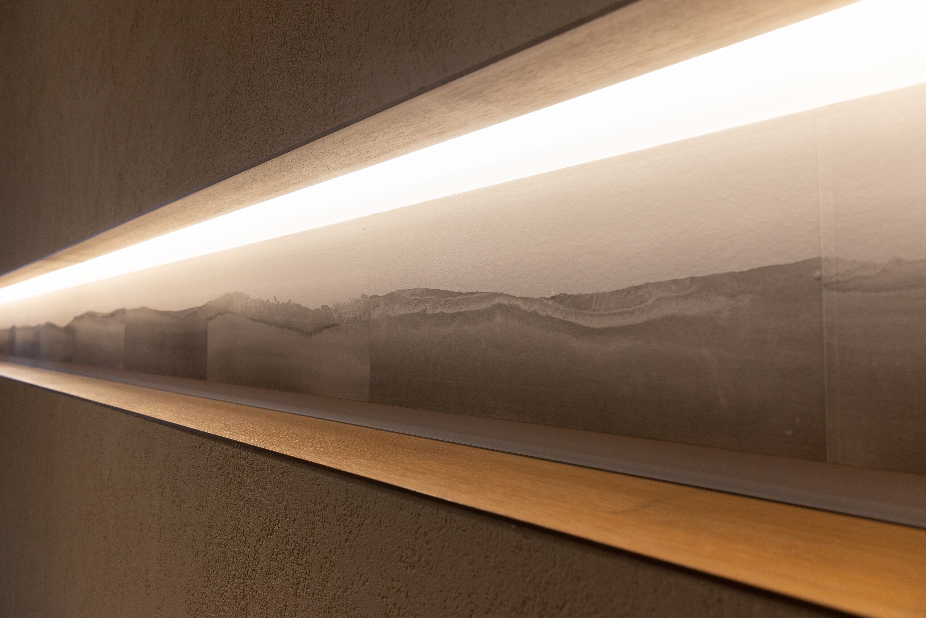 A wall with a framed artwork depicting a mountainous landscape.