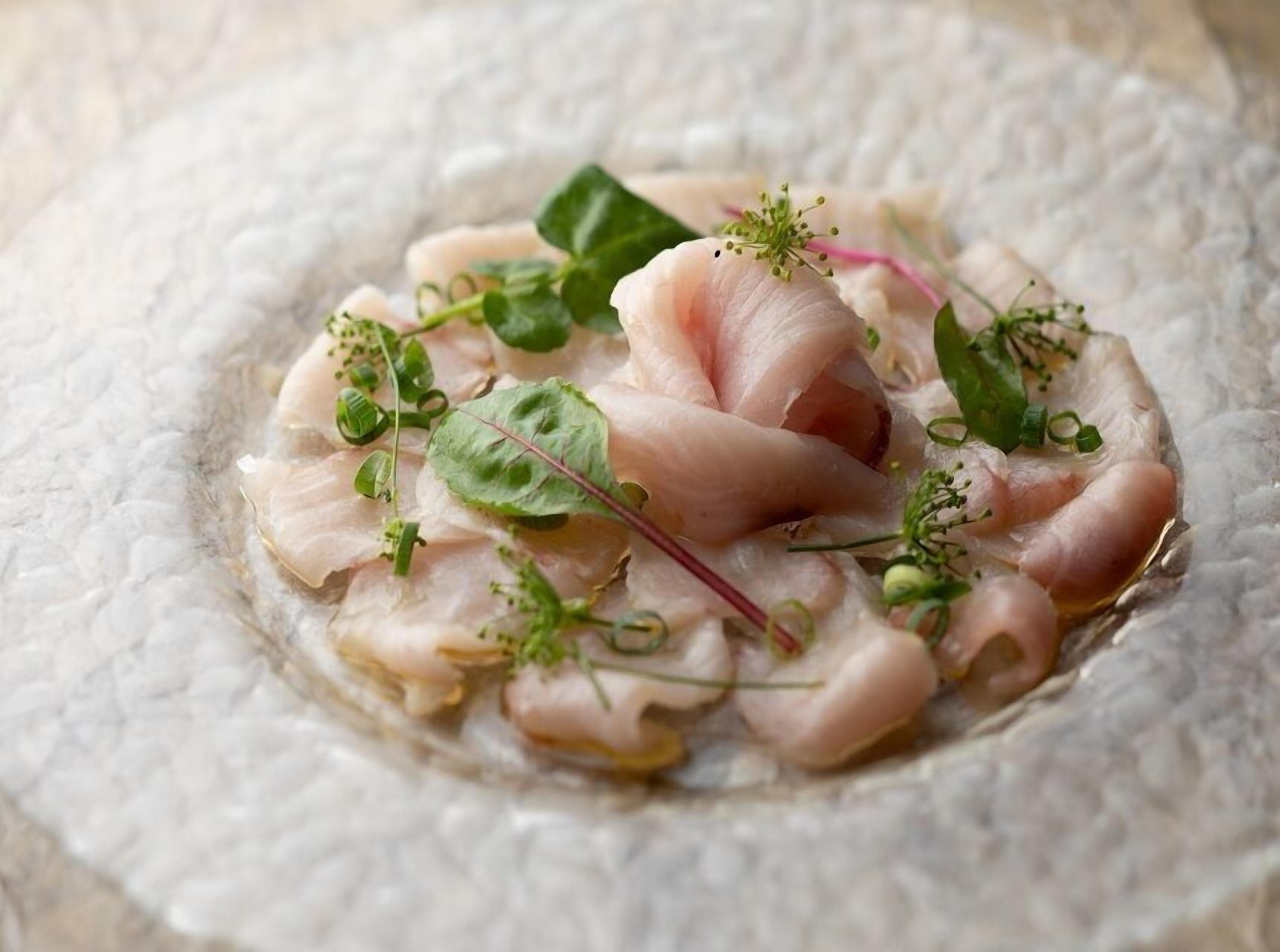 Un plato de pescado crudo adornado con verduras y hierbas.