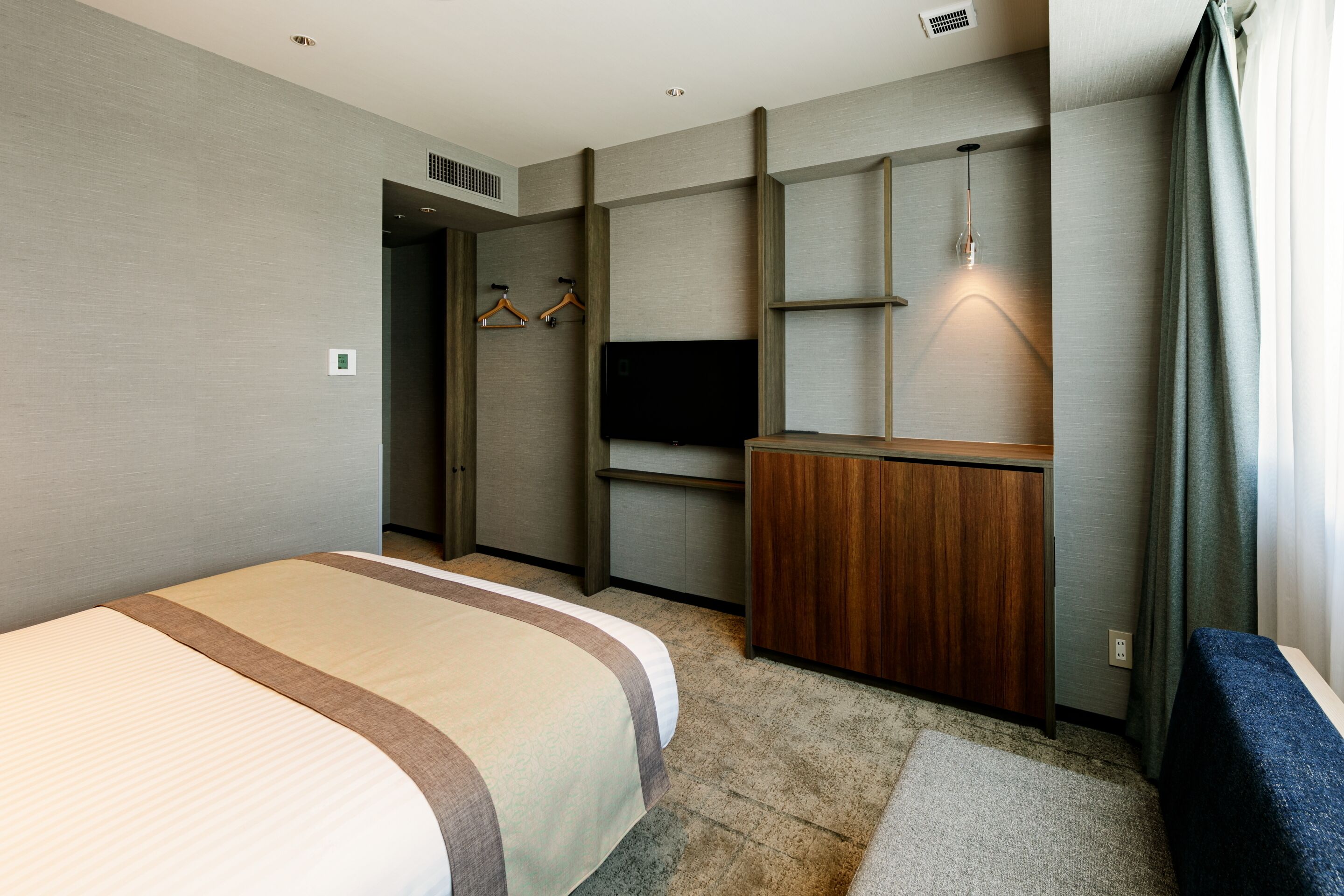 Une chambre d’hôtel avec un grand lit, un bureau en bois, une télévision et une armoire.