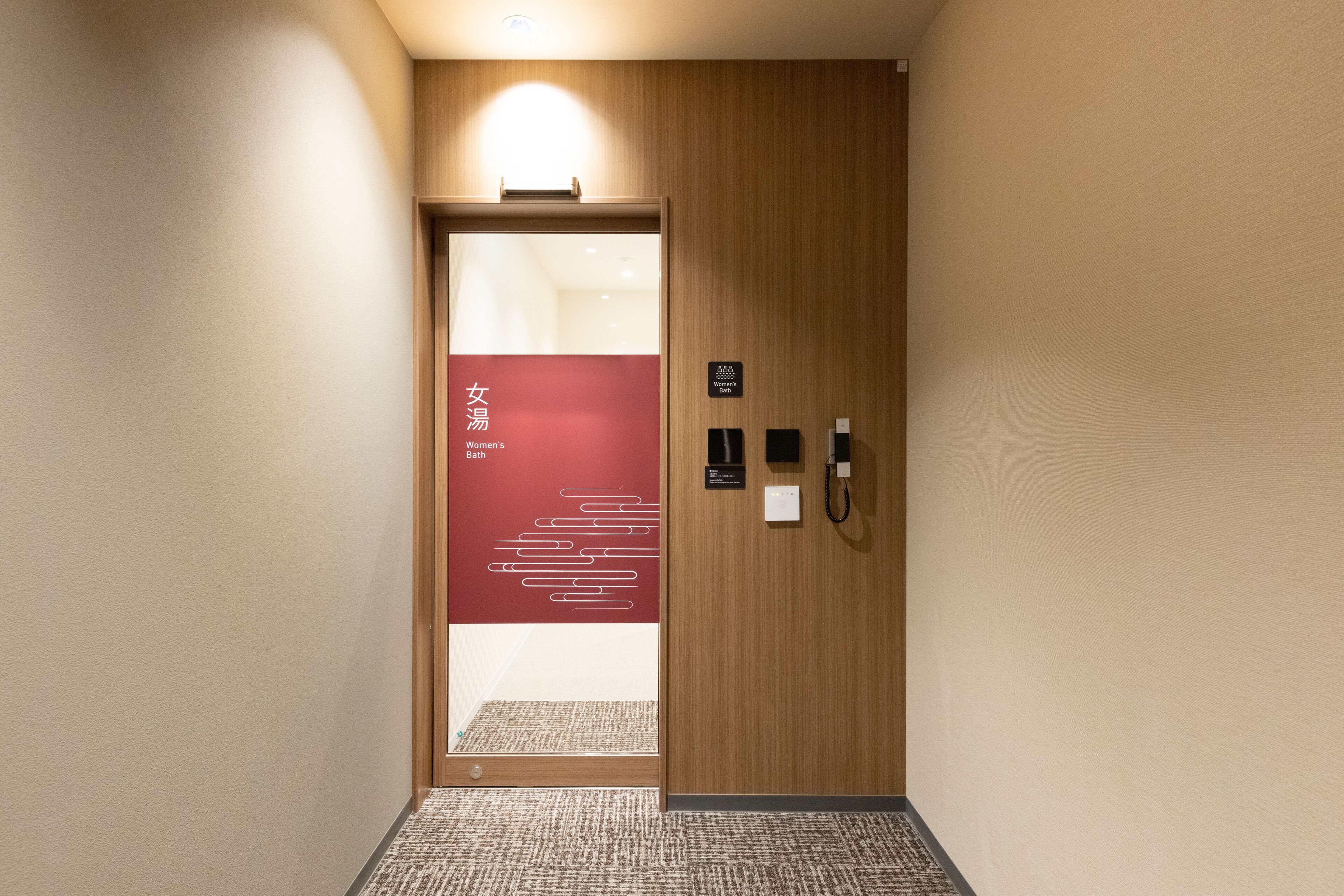 A hotel hallway with a wooden door, a red sign indicating a women's bathroom, and a phone on the wall.