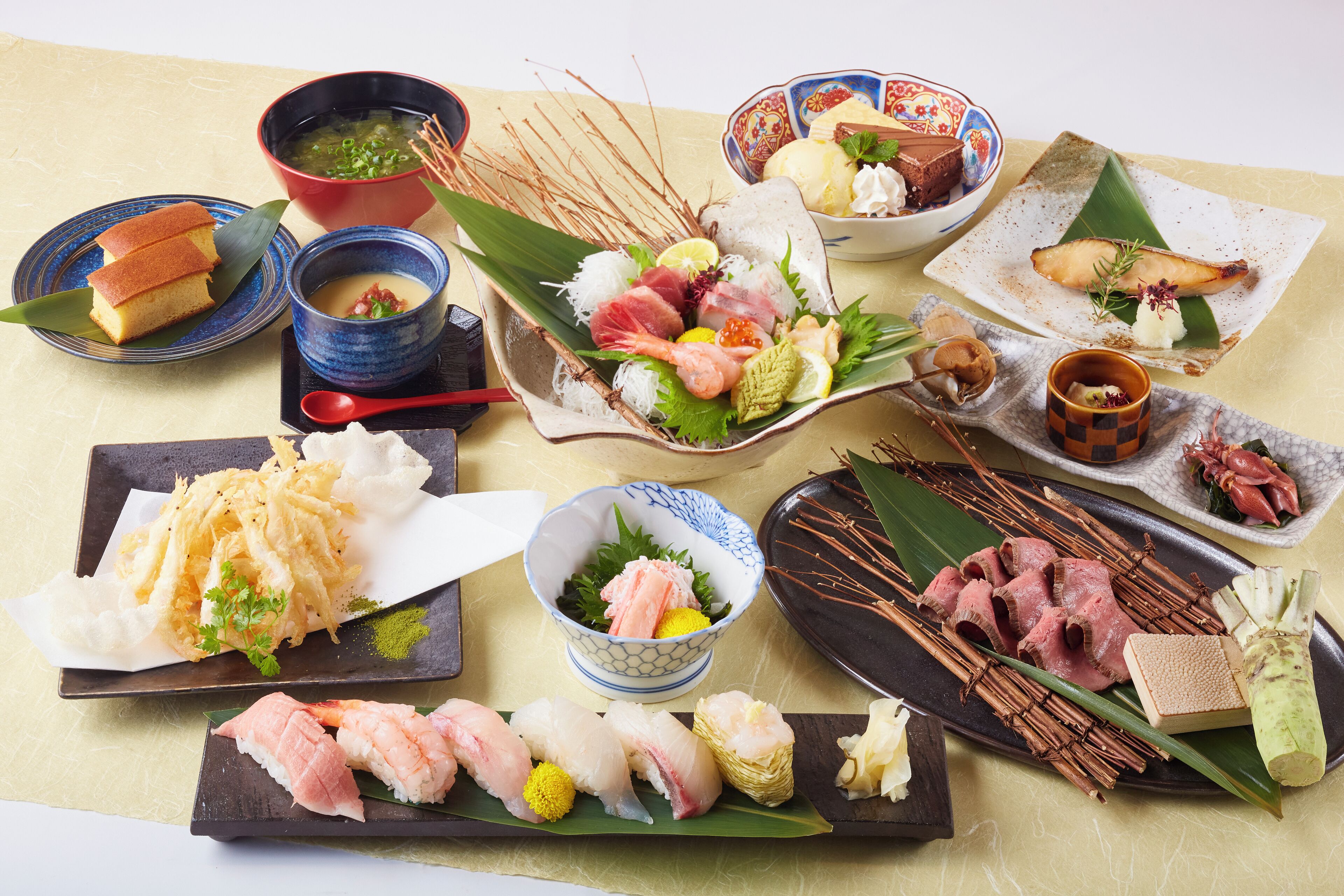 A variety of Japanese dishes including sushi, sashimi, and tempura, arranged on a table with a yellow tablecloth.