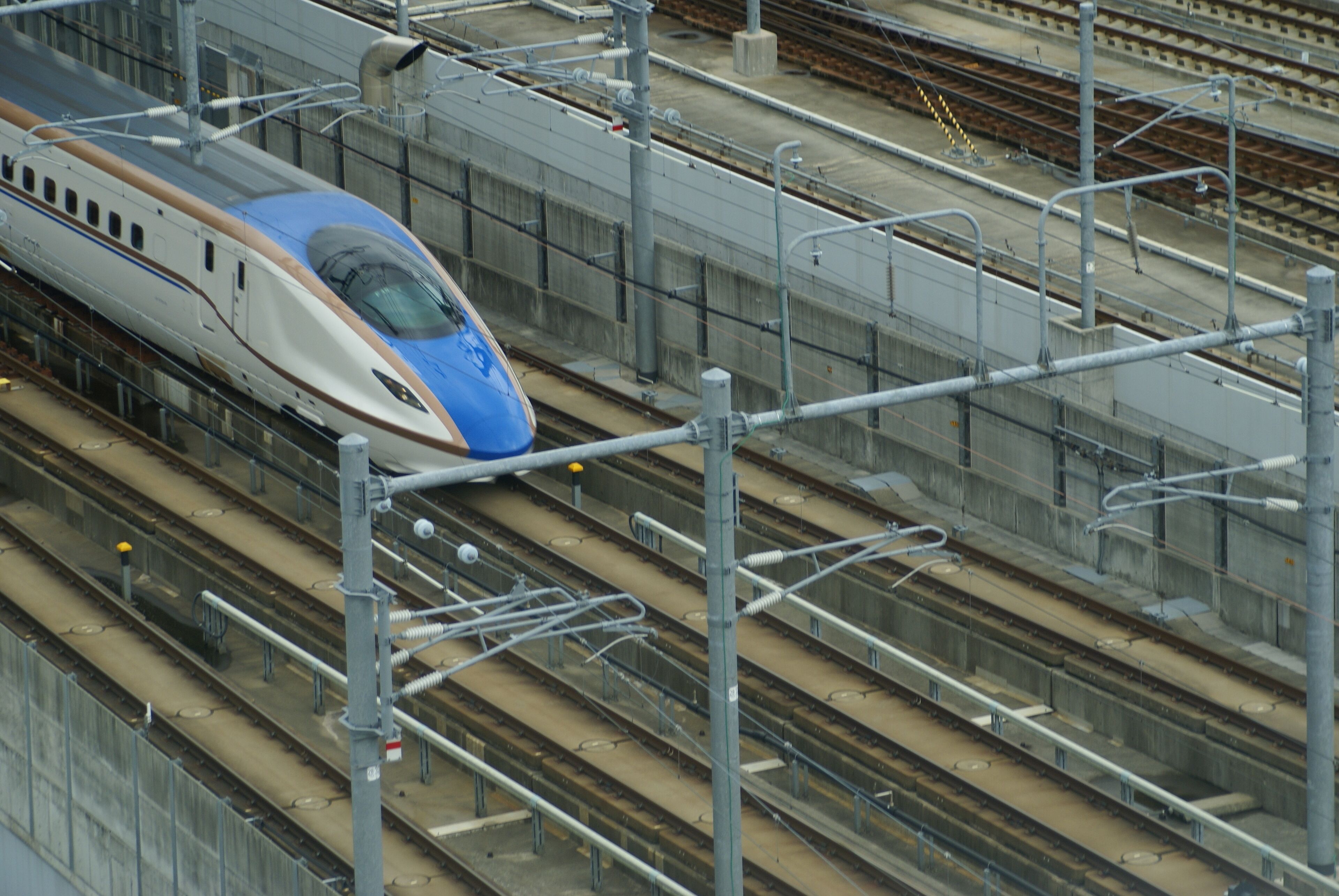 A high-speed train on multiple tracks with overhead electrical lines.