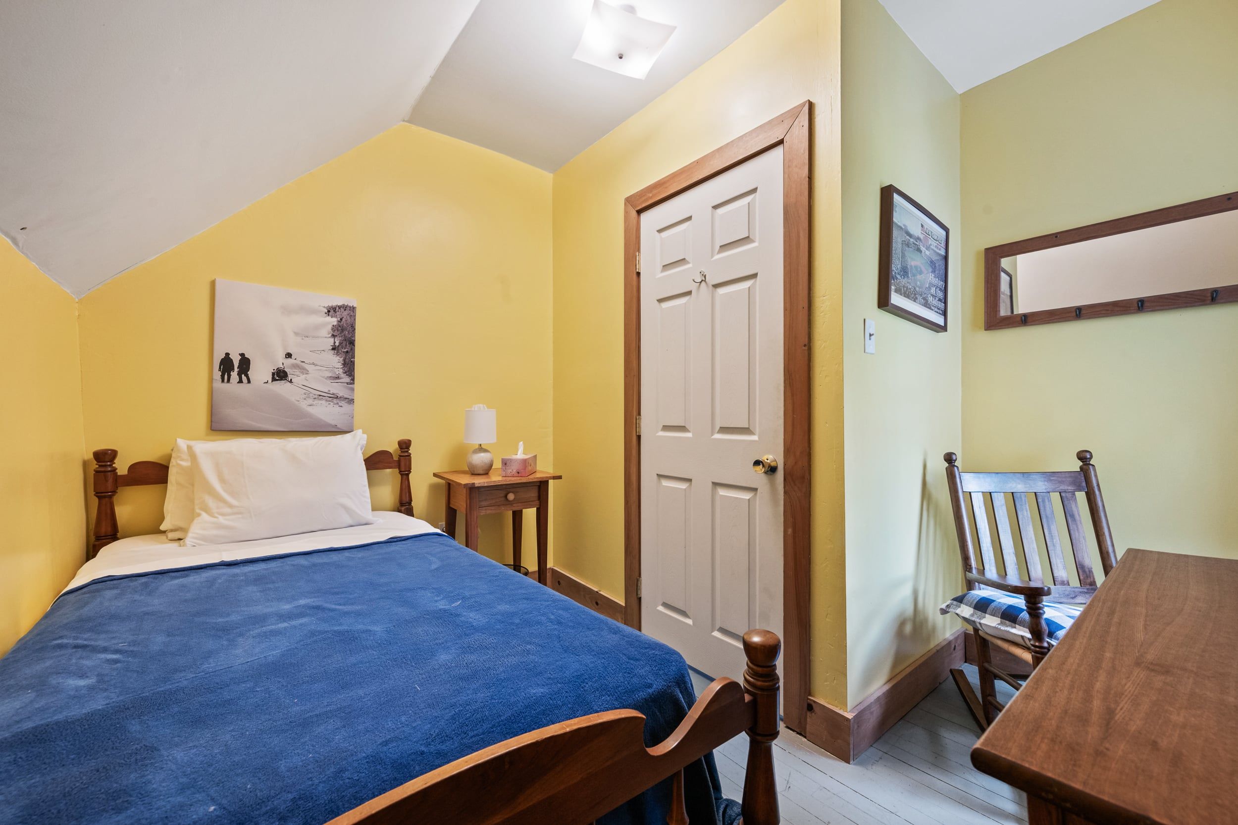 Quarto com cama, mesa de cabeceira com abajur, cadeira e porta.