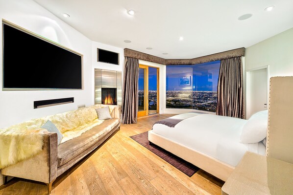Un dormitorio moderno con una cama grande, un sofá, un televisor y vistas a la ciudad.