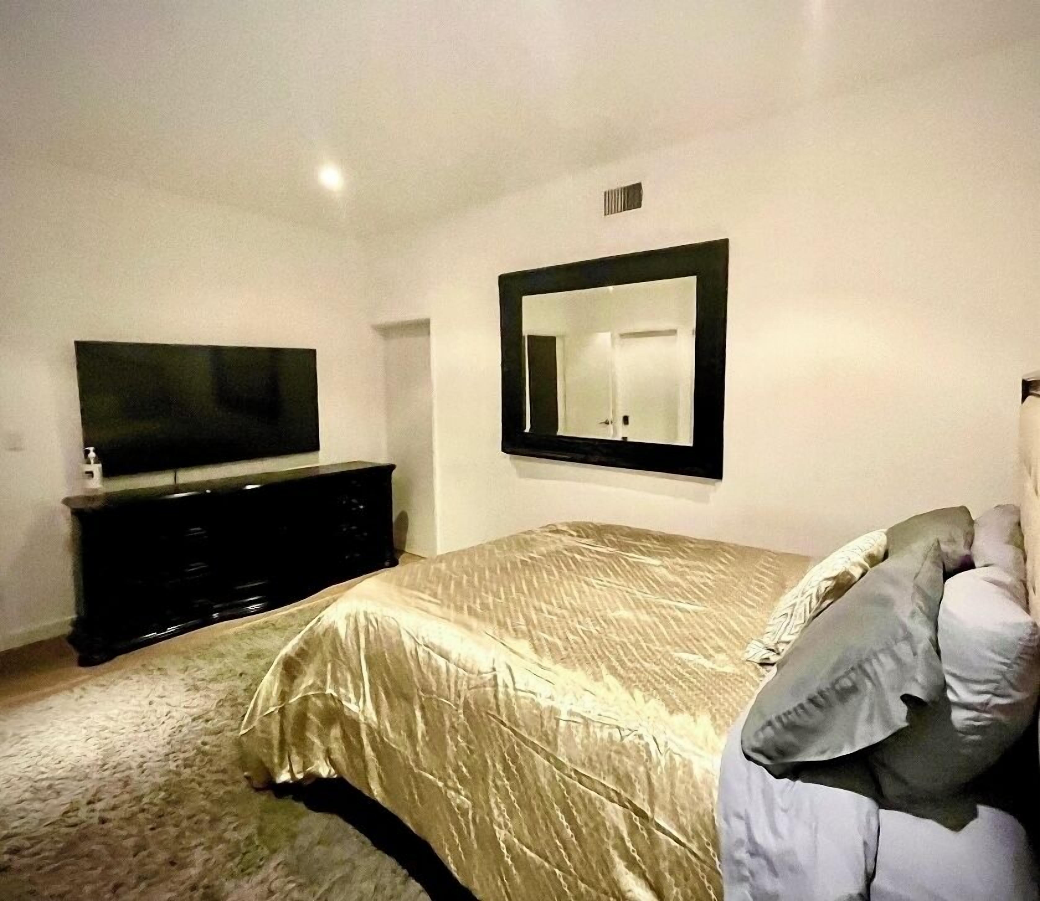 A bedroom with a bed, a dresser, a television, and a mirror.