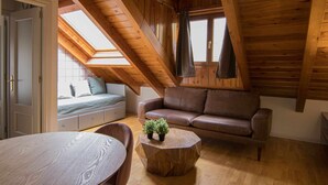 Een gezellig slaapkamer op zolder met een schuine kap, een bruine leren bank, een houten tafel en een kleine potplant.
