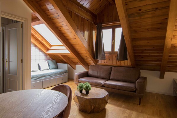 A cozy attic bedroom with a sloped ceiling, a brown leather sofa, a wooden table, and a small potted plant.