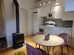 A compact kitchen with a stove, microwave, and dishwasher. There is a round table with chairs and a basket of utensils.